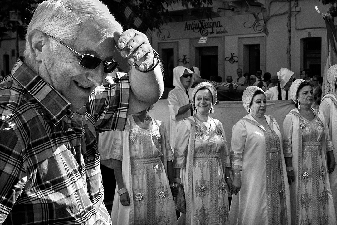 A man adjusting his glasses as a group dressed for a celebration passes by.